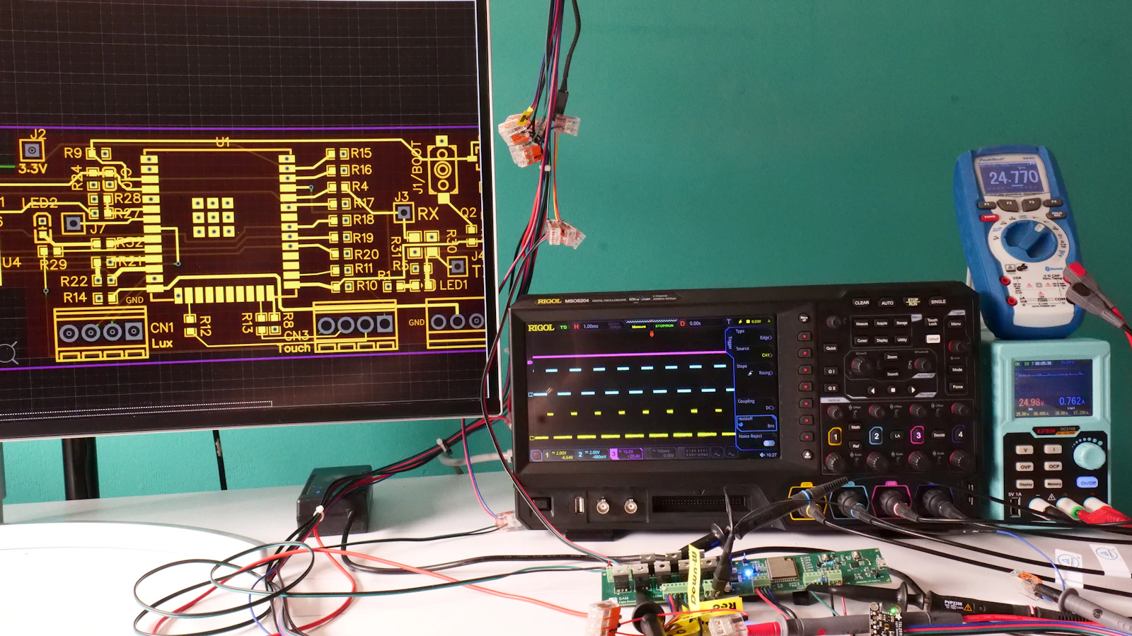 Real electronics workbench with PCB layout display, digital oscilloscope, multimeter and connected test board